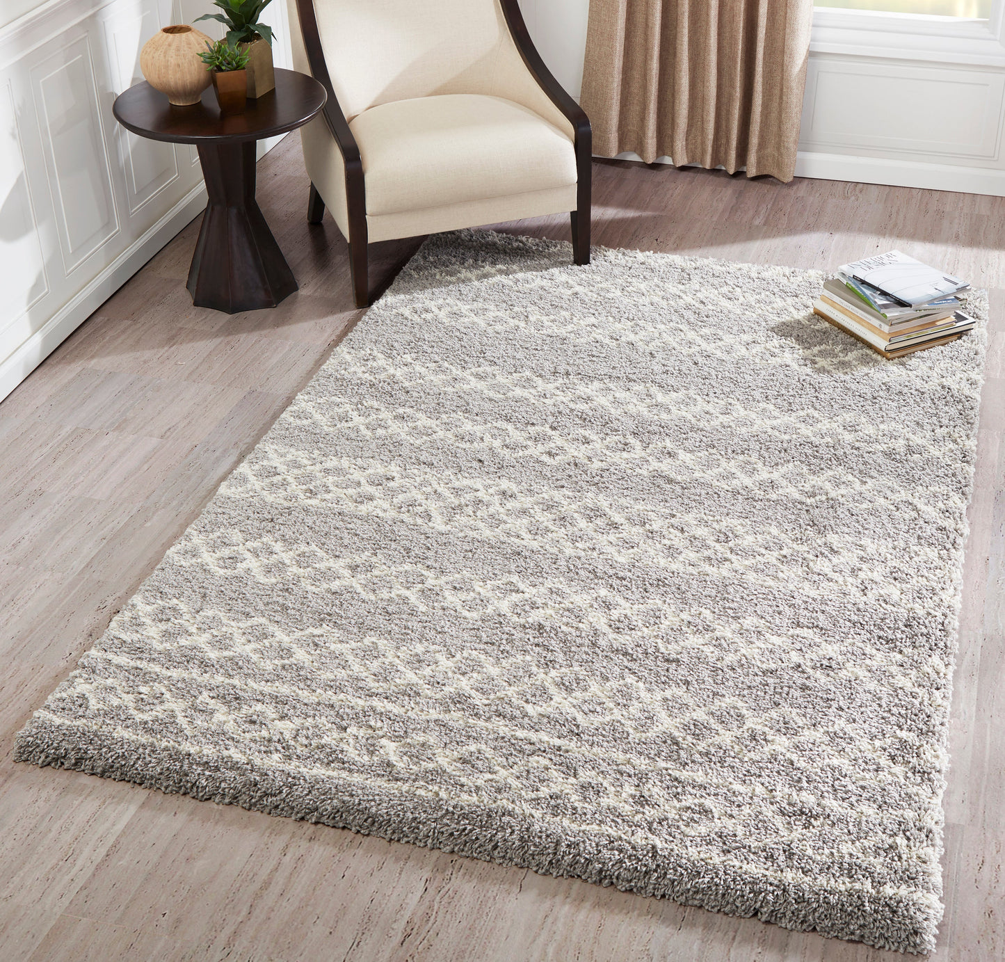 Gray shag area rug with subtle cream geometric pattern under beige armchair and dark wood side table.