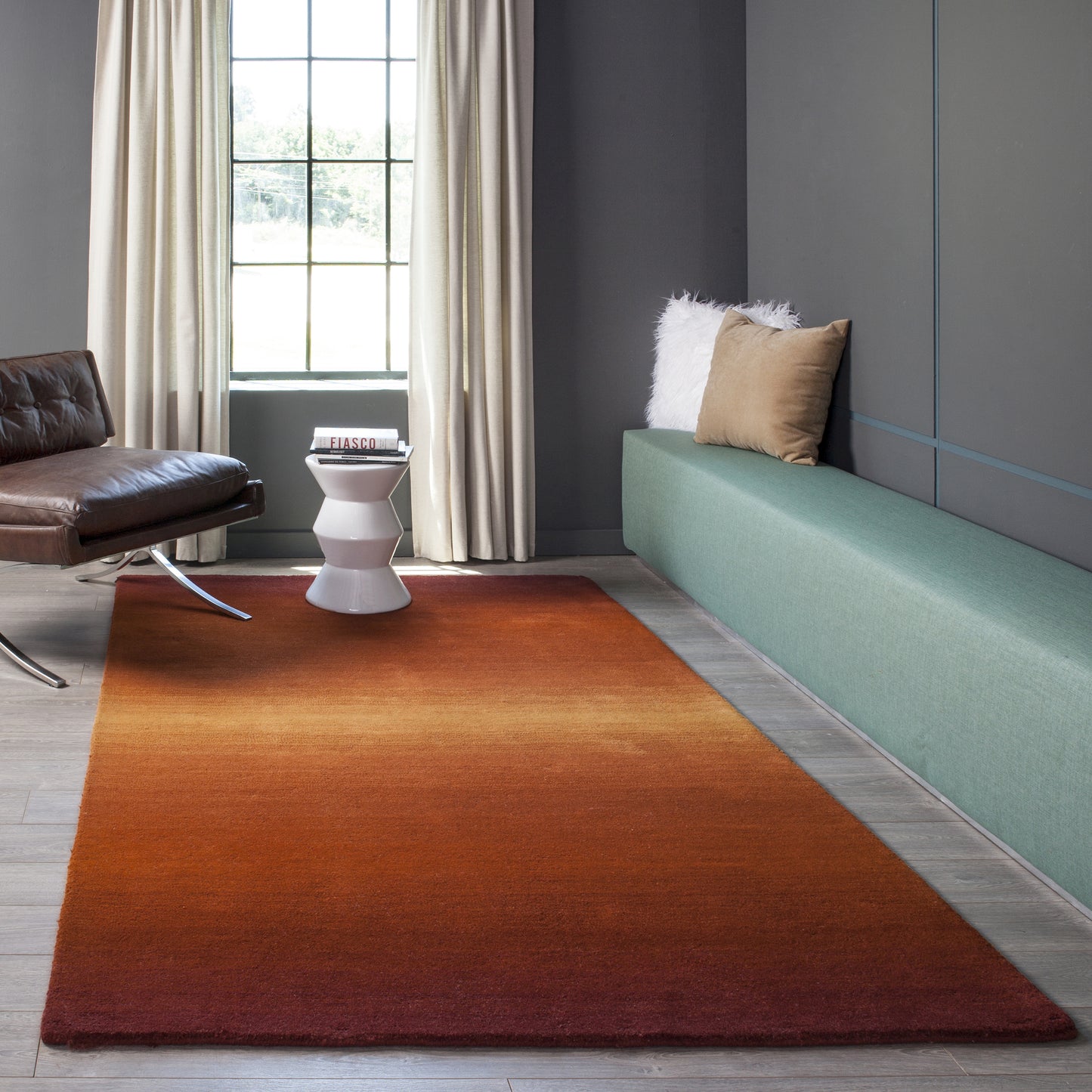 Living room with gradient orange-to-red rug, green built-in bench, brown leather lounge chair, white side table, beige curtains.