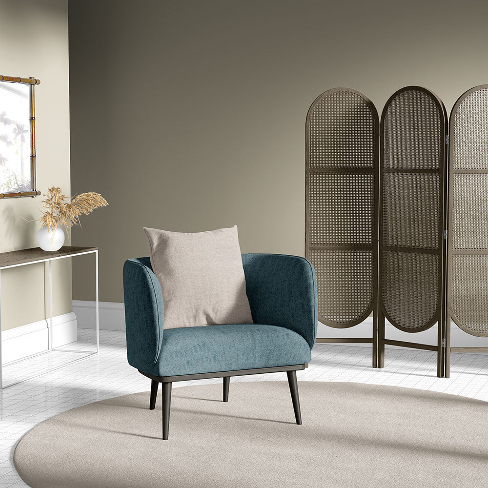 Teal fabric accent chair with beige cushion and dark wood legs in a modern living room with a woven folding screen.