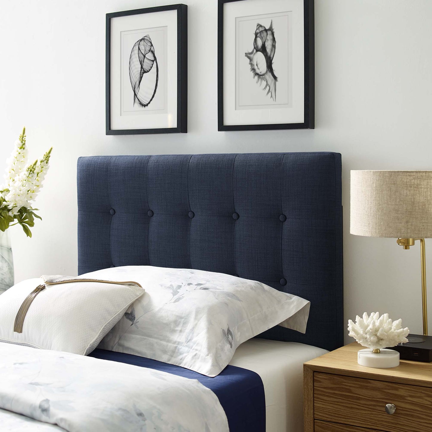 Navy tufted upholstered twin headboard with white-and-blue bedding; two framed botanical prints above; wood nightstand with lamp.