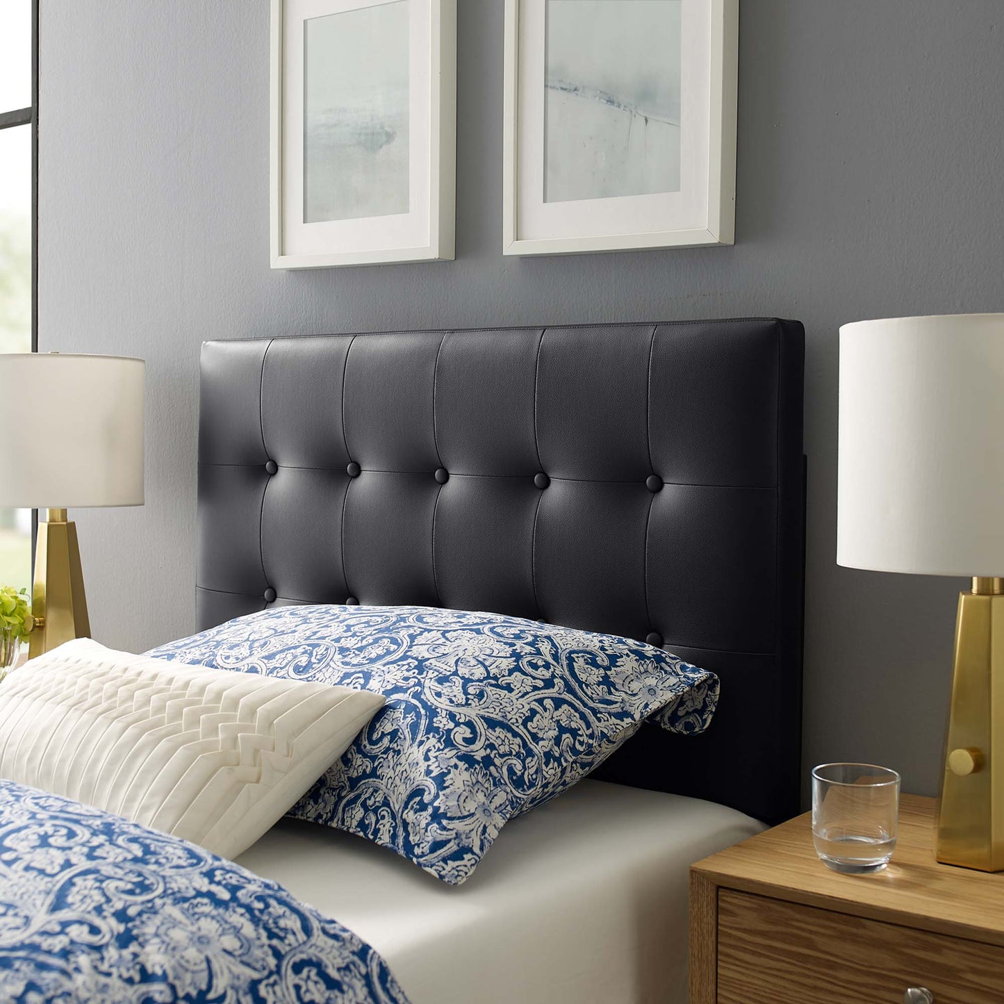 Black tufted headboard with blue damask bedding, white quilted pillow, and gold-lamped nightstands with framed art