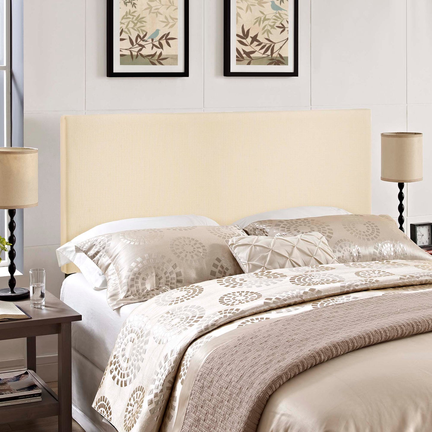 Ivory upholstered queen headboard; part of a bed setup with a beige patterned duvet, decorative pillows, two lamps and framed botanical art.