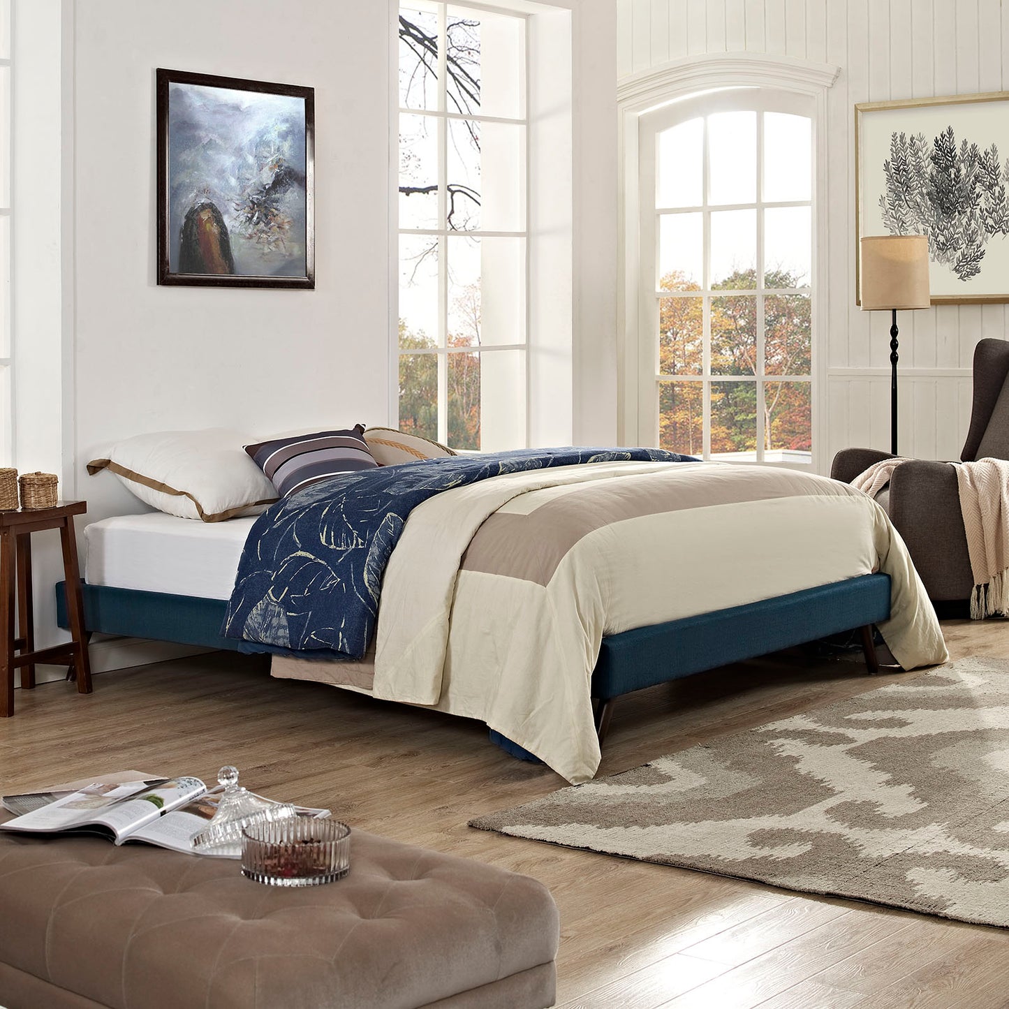 Azure fabric queen bed frame with beige duvet and navy patterned quilt in a bright, window-filled bedroom.