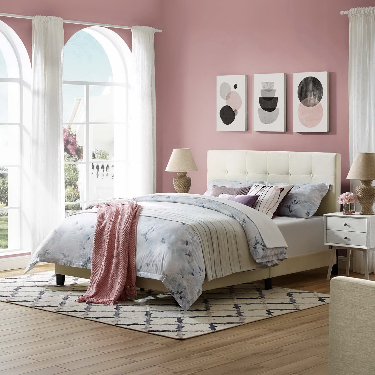 Pastel pink bedroom with ivory tufted button upholstered performance velvet full platform bed, blue floral duvet, pink throw, white curtains, arched windows, abstract art.