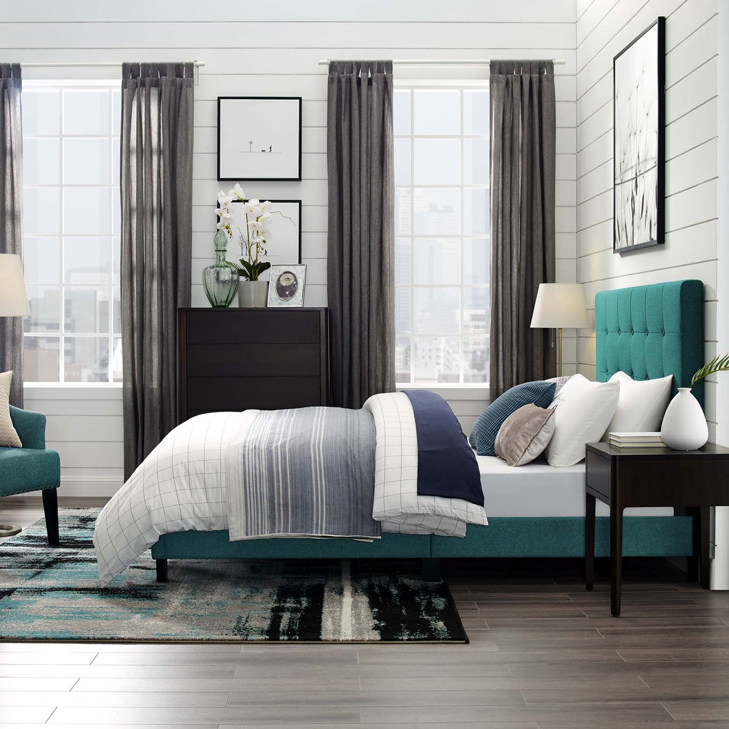 Teal upholstered bed with white and blue bedding, dark wood dresser, and gray curtains in a modern bedroom.