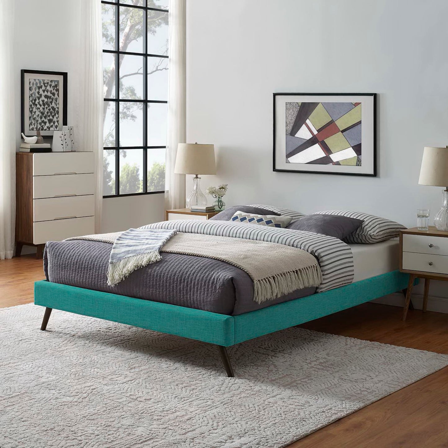 Teal fabric full bed frame with dark gray bedding, beige throw, striped sheets; nightstands, glass lamps, abstract art.