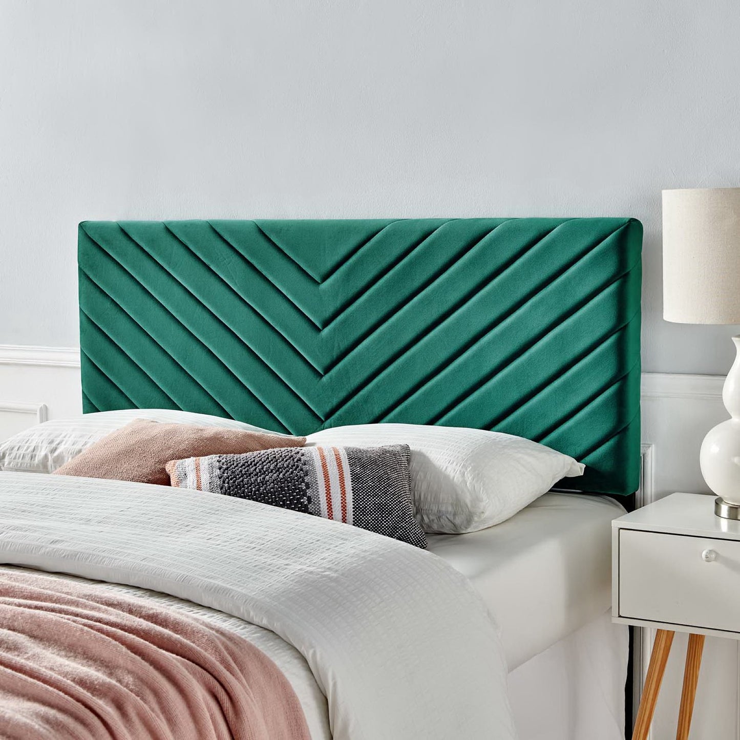 Teal velvet chevron headboard with diagonal stitching, white bedding, pink throw & white nightstand with lamp.