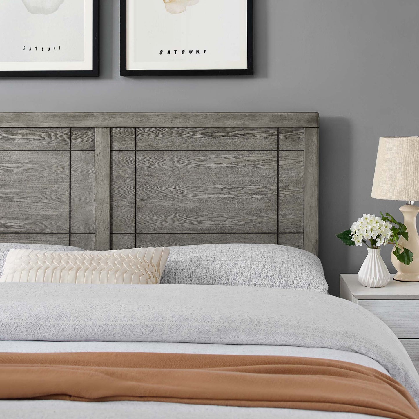 Weathered gray wood headboard with light-gray bedding, rust throw at foot, beige pleated pillow, white nightstand with lamp.