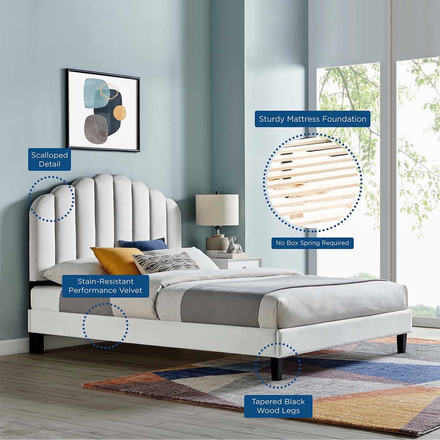 Light gray velvet upholstered platform bed with scalloped headboard and tapered black wood legs in a blue-toned bedroom.