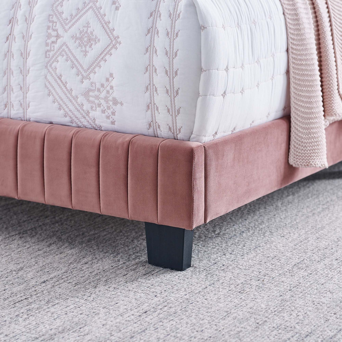 Red velvet twin bed with vertical channel tufting & black block legs, paired with a white embroidered quilt.