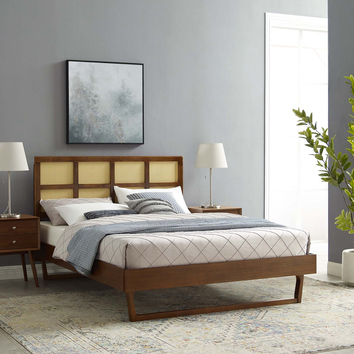 Walnut wood king platform bed with a cane headboard, gray bedding, matching nightstands, and lamps in a mid-century modern bedroom setup.