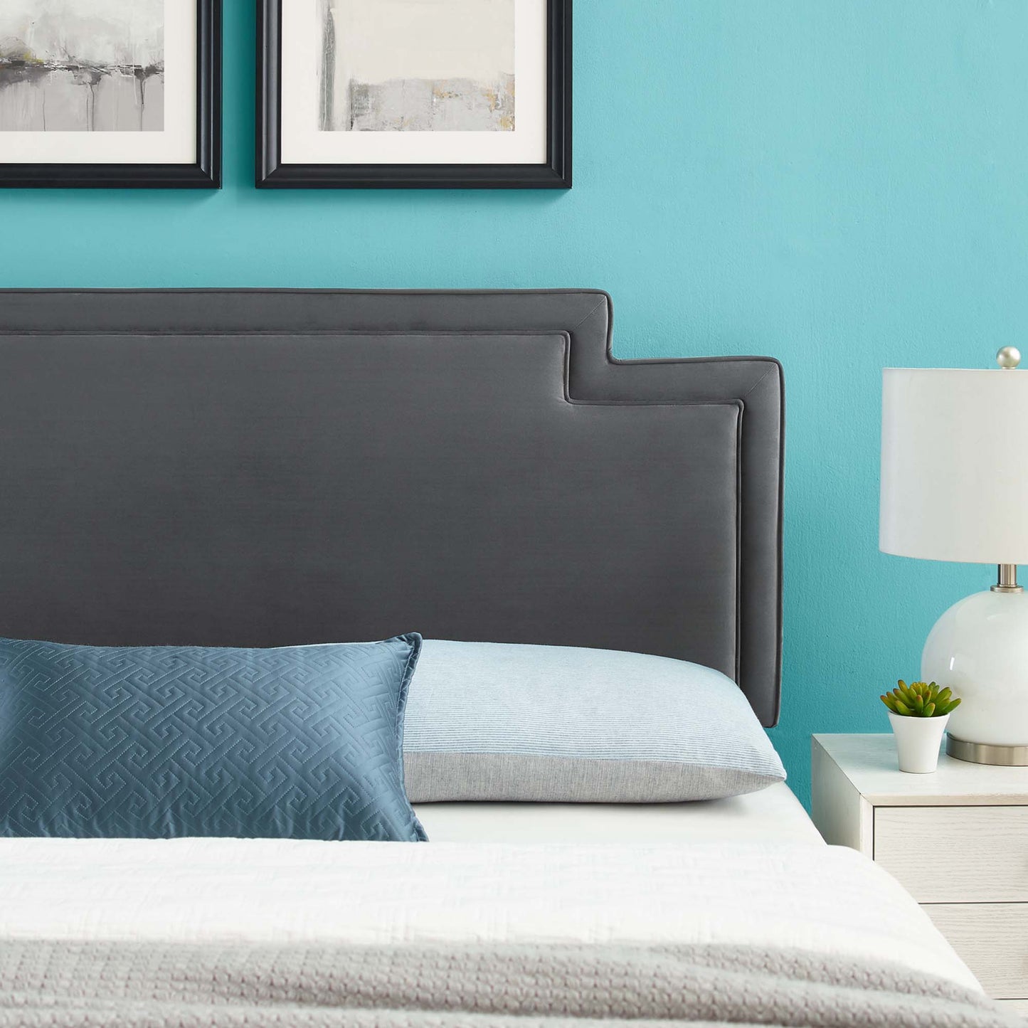 Charcoal upholstered headboard with a stepped design against teal wall; blue patterned pillow, light gray pillow, white bedding.