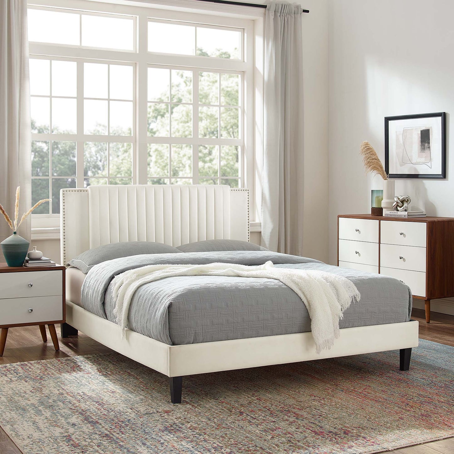 White upholstered twin platform bed with channel tufted headboard; gray bedding; midcentury nightstands and dresser in a bright bedroom.