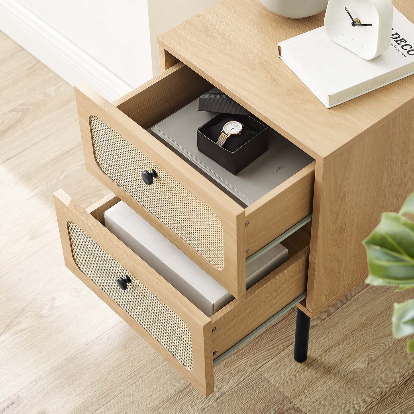 Oak nightstand with two cane-front drawers; top drawer open holds a watch box, with a clock and book on top.