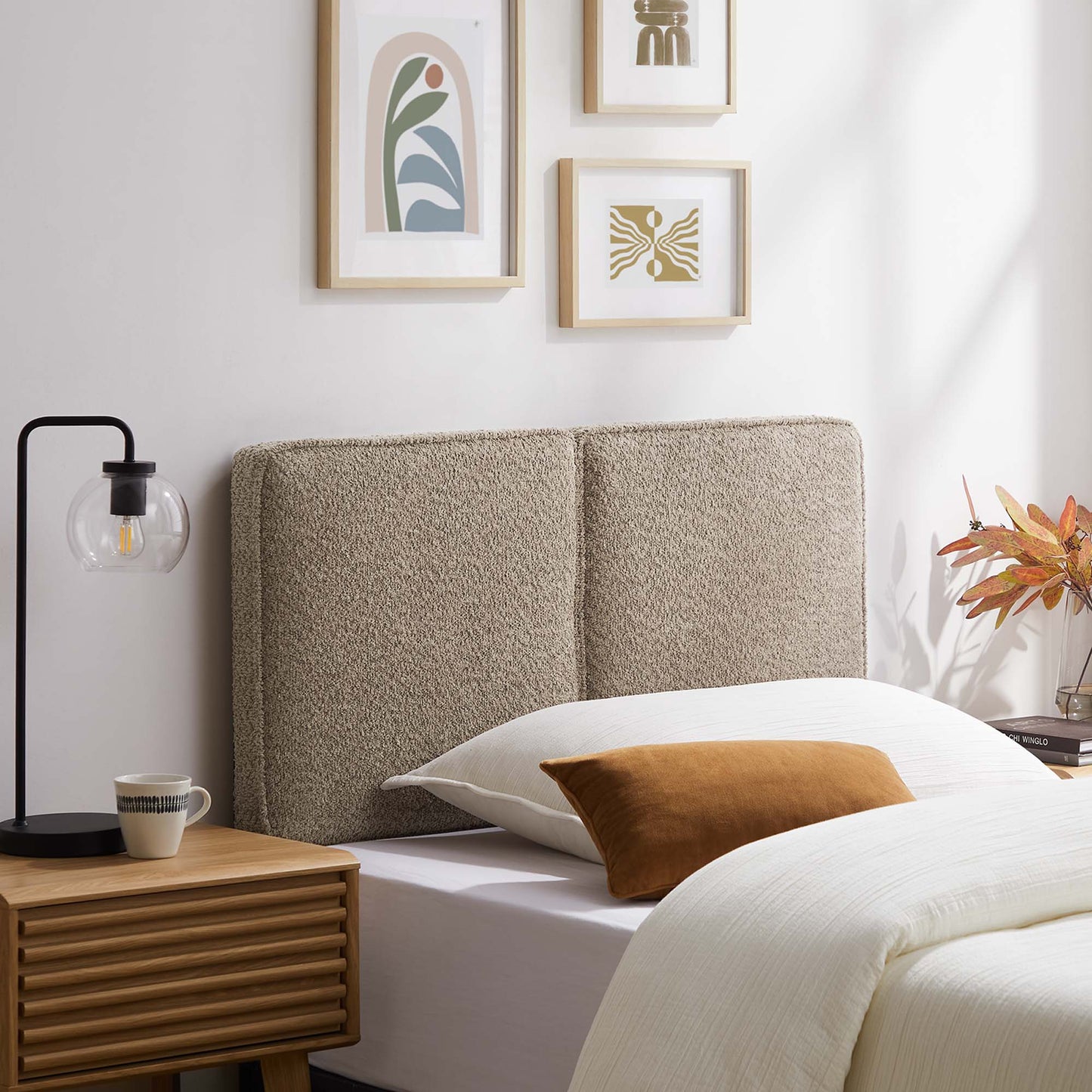 Oatmeal boucle upholstered bed headboard with wooden nightstand, white bedding, orange pillow, modern wall decor.