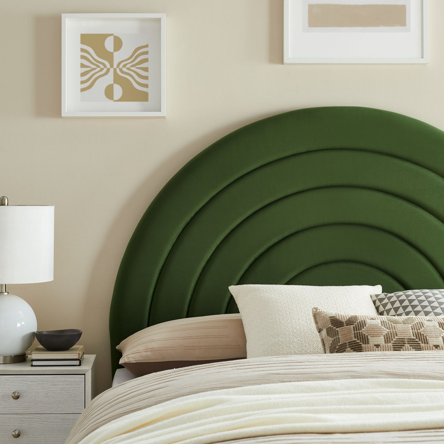 Deep green curved upholstered headboard with layered arches, beige bedding, white nightstand, lamp, and neutral wall art.