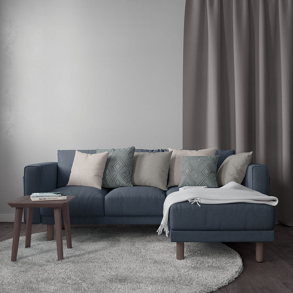 Blue-gray sectional sofa with beige and teal patterned cushions, light throw, wooden side table, gray curtains, cozy living room.