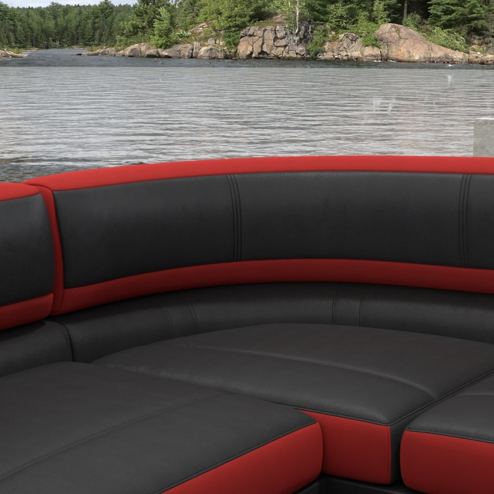 Curved seating upholstered in red solid fabric with cushioned backrests, shown beside a lake with a rocky shoreline and trees in the background.
