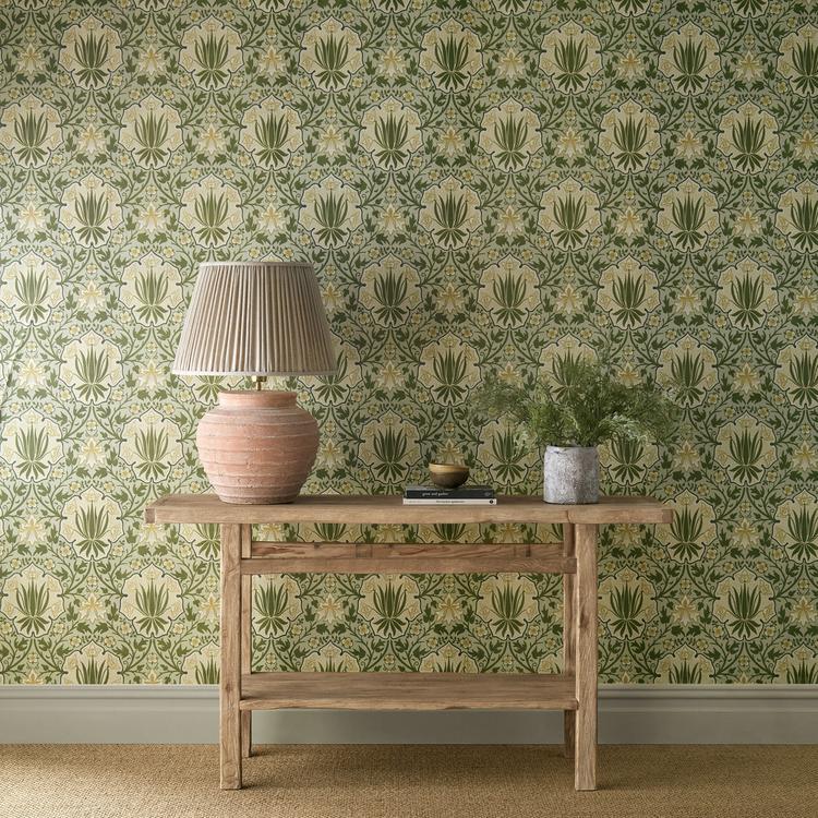Luxury botanical floral wallpaper featuring iris flowers, roses, shield motifs, and trailing vines in Bayleaf/Weld green and gold tones by Morris & Co. Vintage English cottage wallpaper ideal for Victorian interiors, maximalist homes, dining rooms, bedrooms, powder rooms, and elegant statement walls.