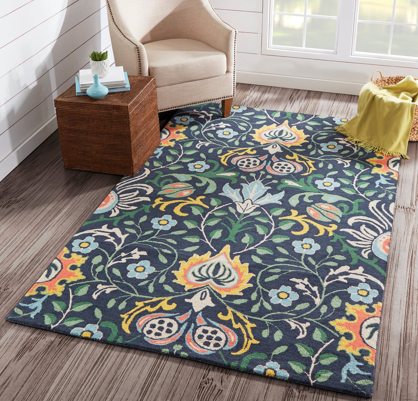 Navy background floral area rug with multicolor blossoms in teal, yellow, and orange beside a beige upholstered armchair.