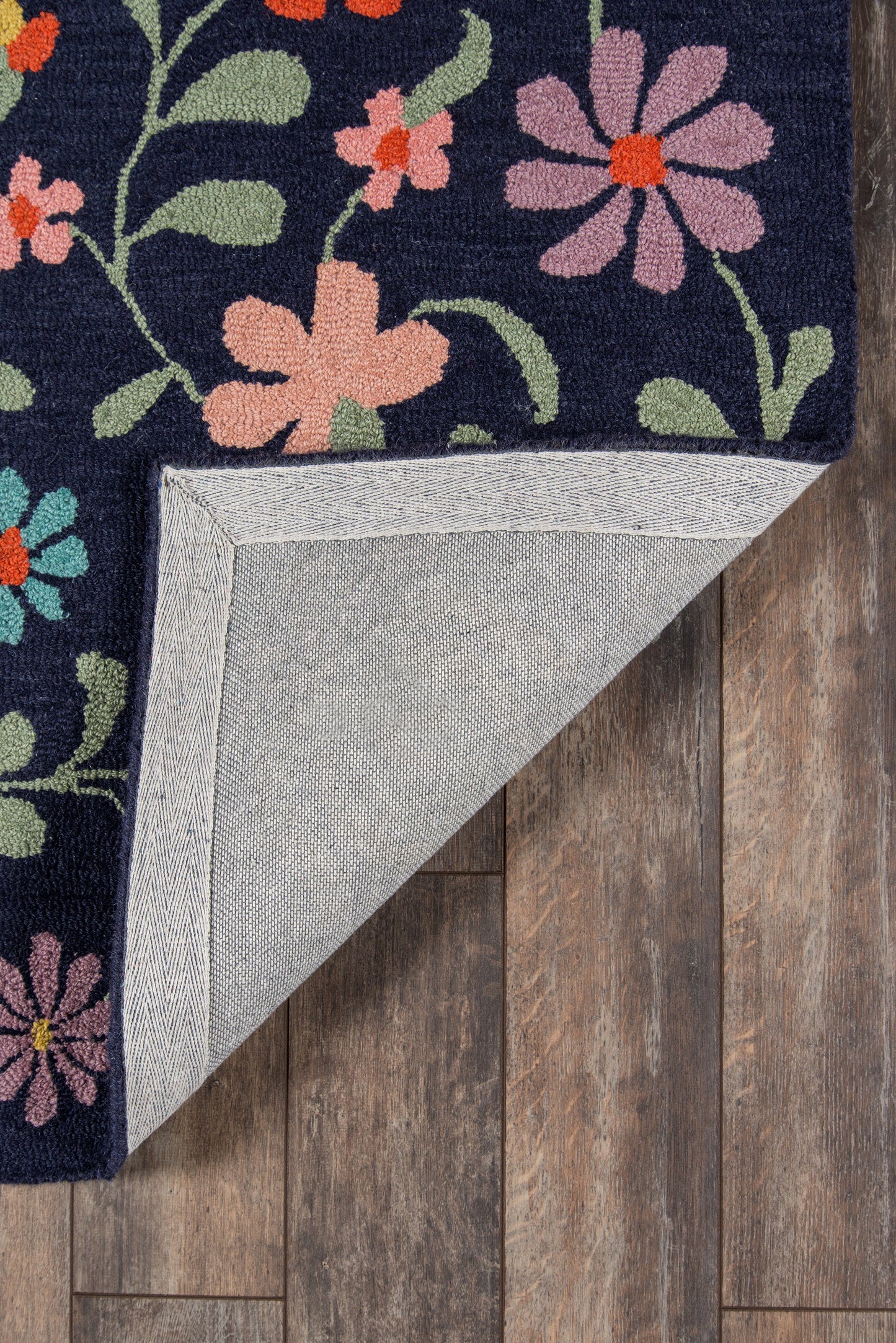 Navy rug with bright pink, coral and green floral pattern; folded corner shows light gray backing on wooden floor.