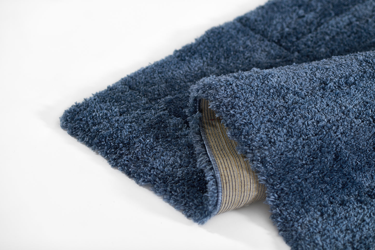 Indigo blue plush shag rug with striped beige backing; cozy microfiber texture, bath-mat ready.