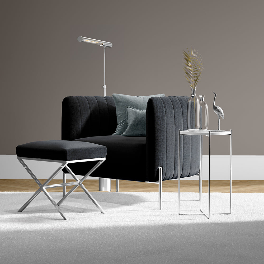 Charcoal velvet sofa with curved channel arms, matching ottoman, chrome legs, and glass side tables in a modern living room.