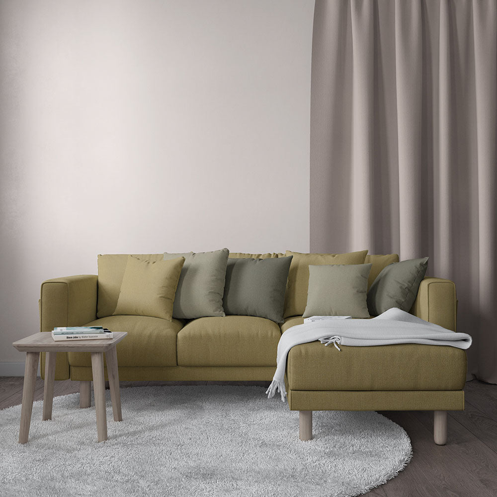 Mustard-yellow fabric sectional with chaise, assorted green/gray cushions, light wood legs, throw on gray rug.