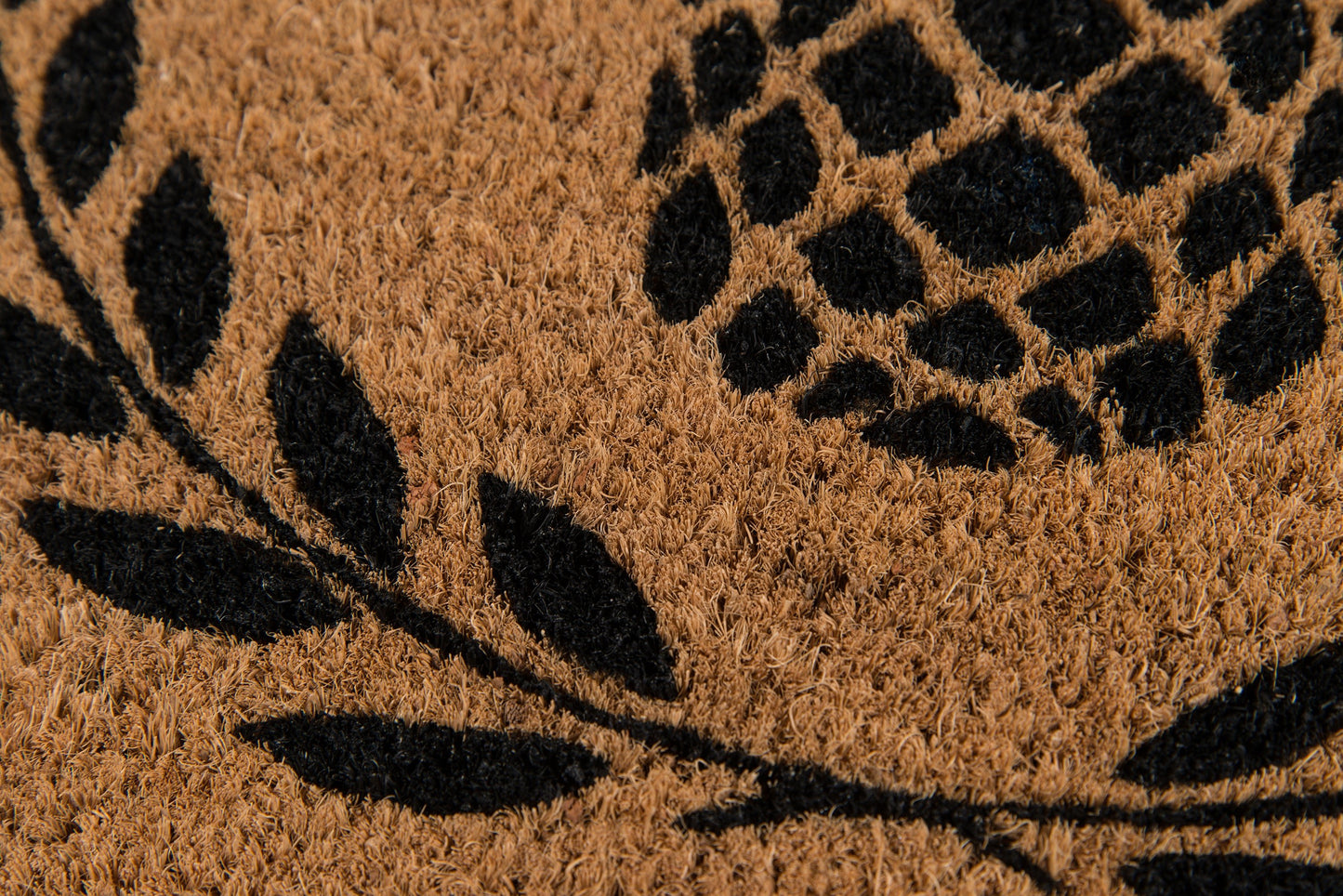 Natural brown coir doormat with black botanical leaves and a circular dotted cluster motif.