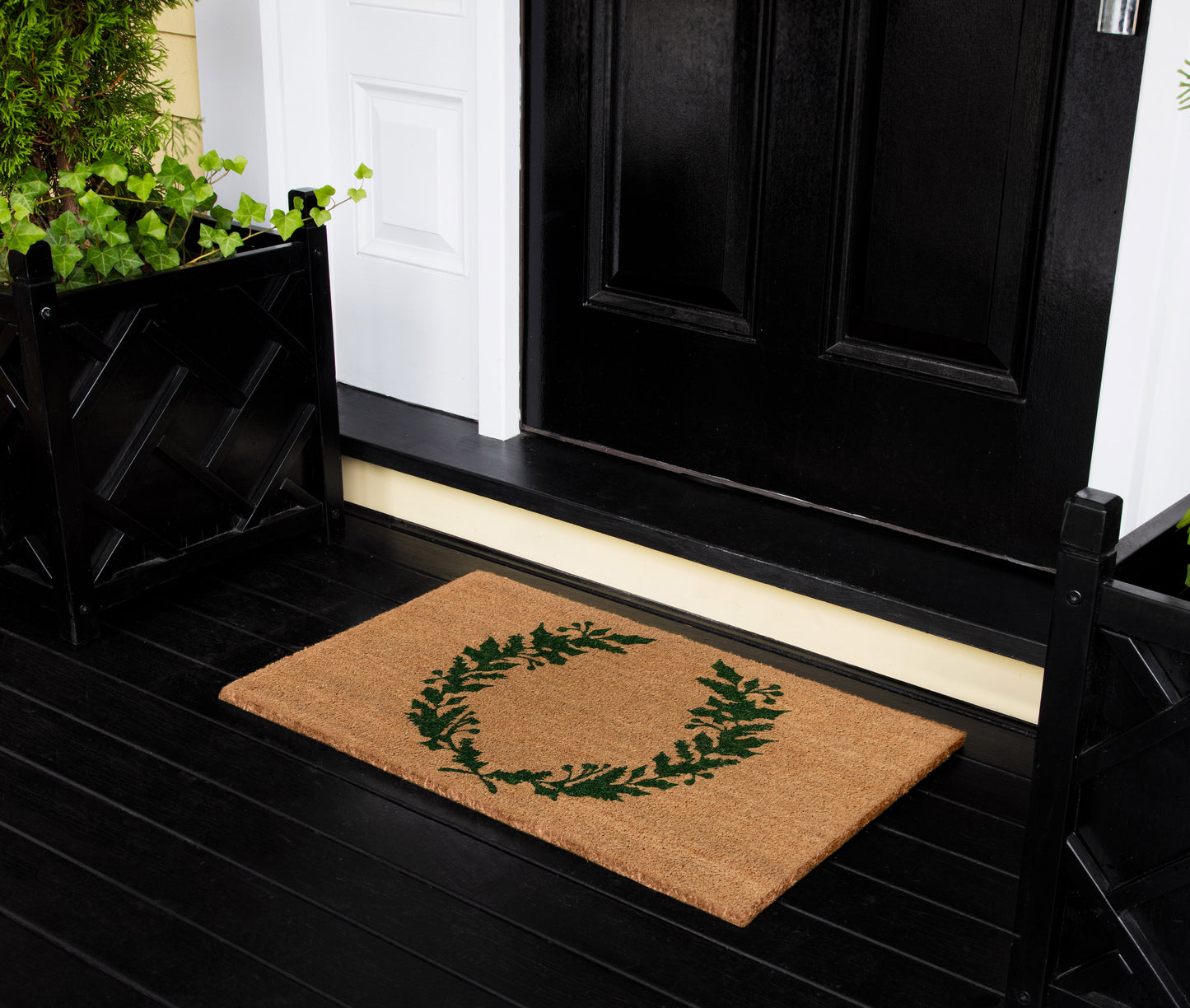 Brown coir rug with a green leafy wreath motif on a black front porch.