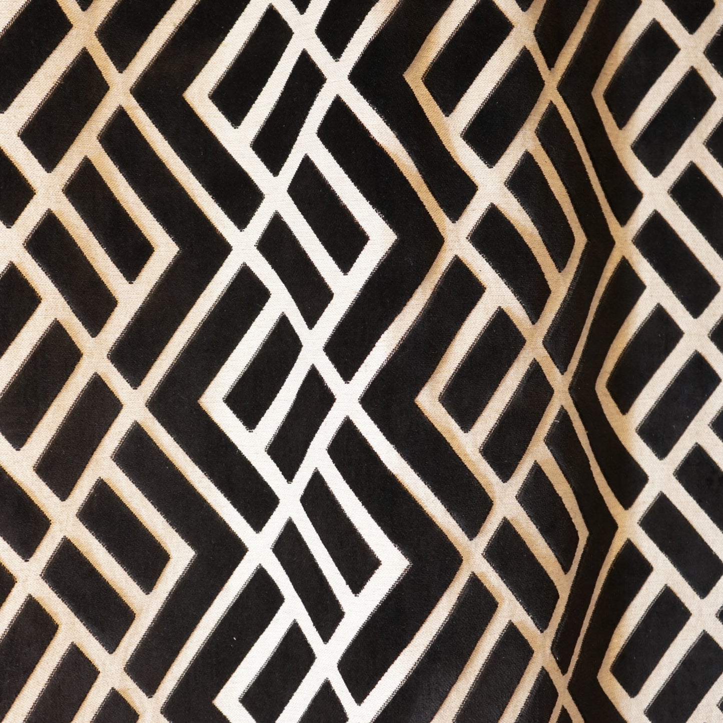 Close-up of black fabric with cream-beige geometric lattice of interlocking diamonds.