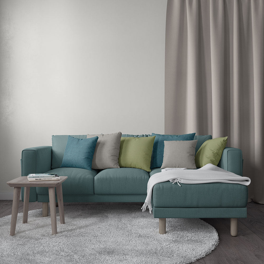 Teal sectional sofa with chaise in living room, multicolored cushions, grey throw, wooden side table with magazines.