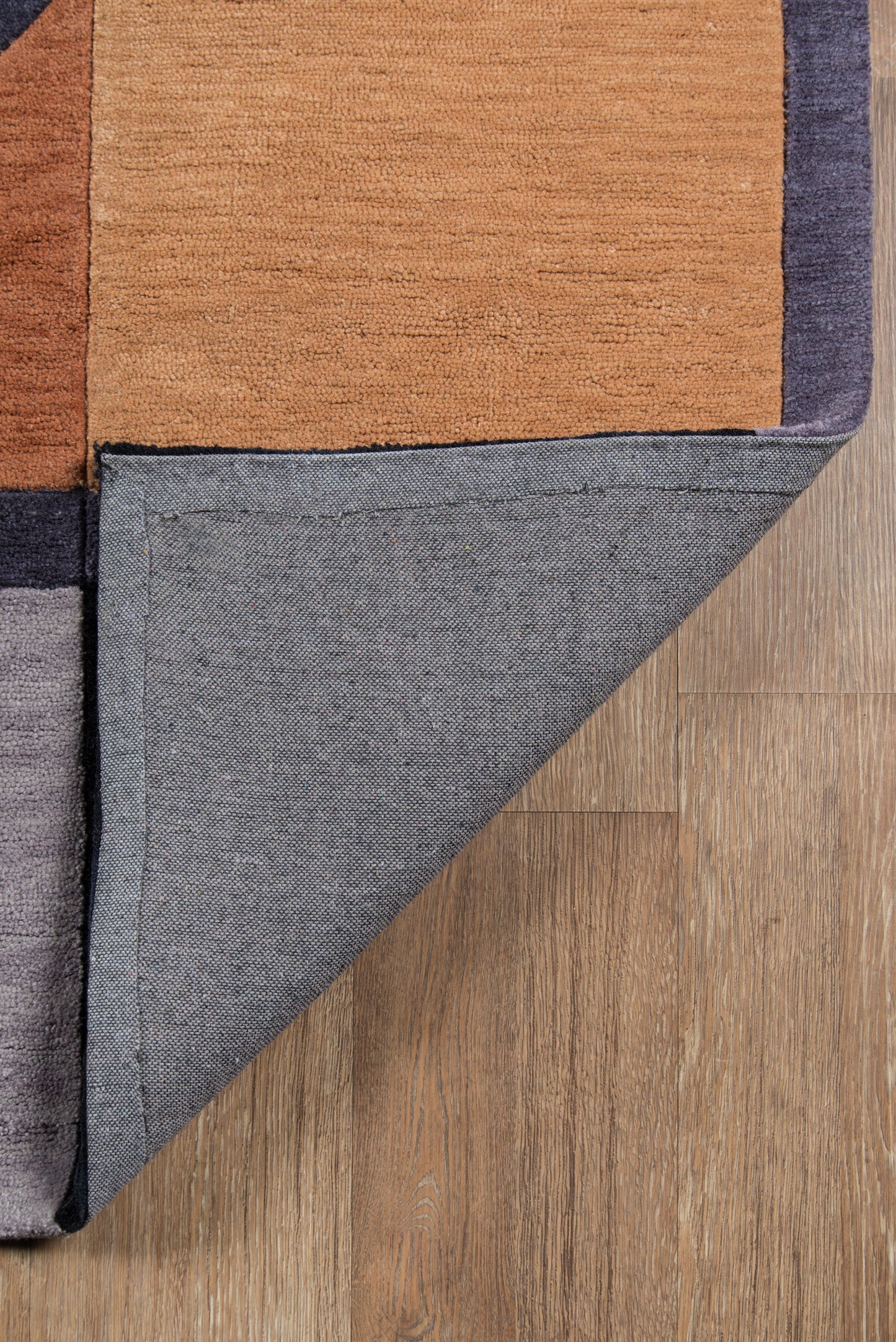 Geometric color-block rug in orange, navy and charcoal; folded corner shows grey underside on wood floor.