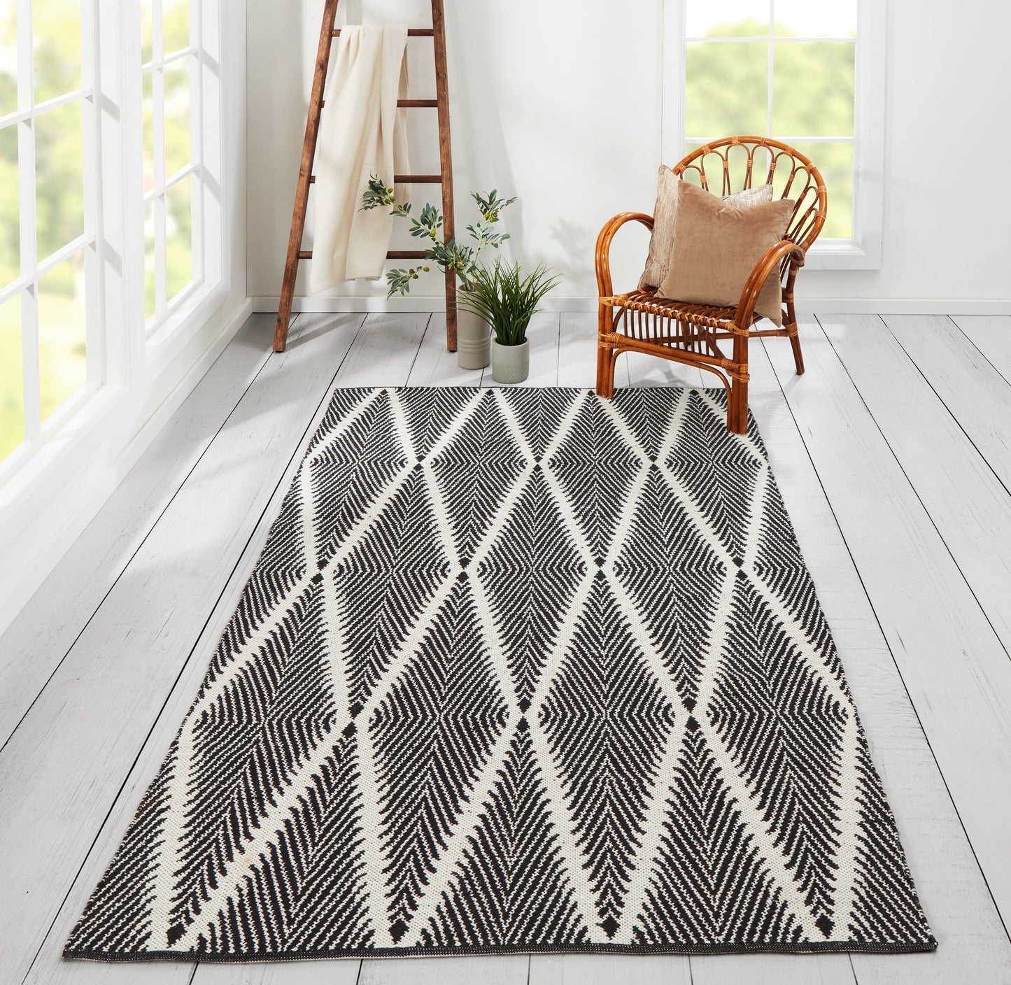 Black-and-white geometric rug with diamond chevron pattern in a bright room; wicker chair, ladder, and plants.