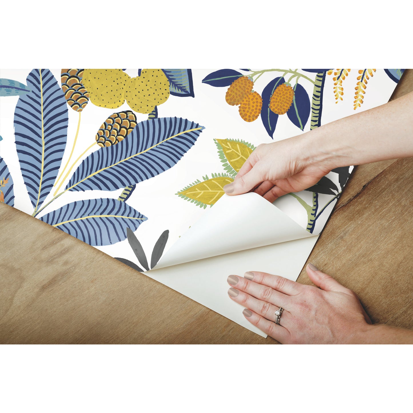 Self-adhesive wallpaper featuring blue leaves and yellow fruit, being peeled from white backing.