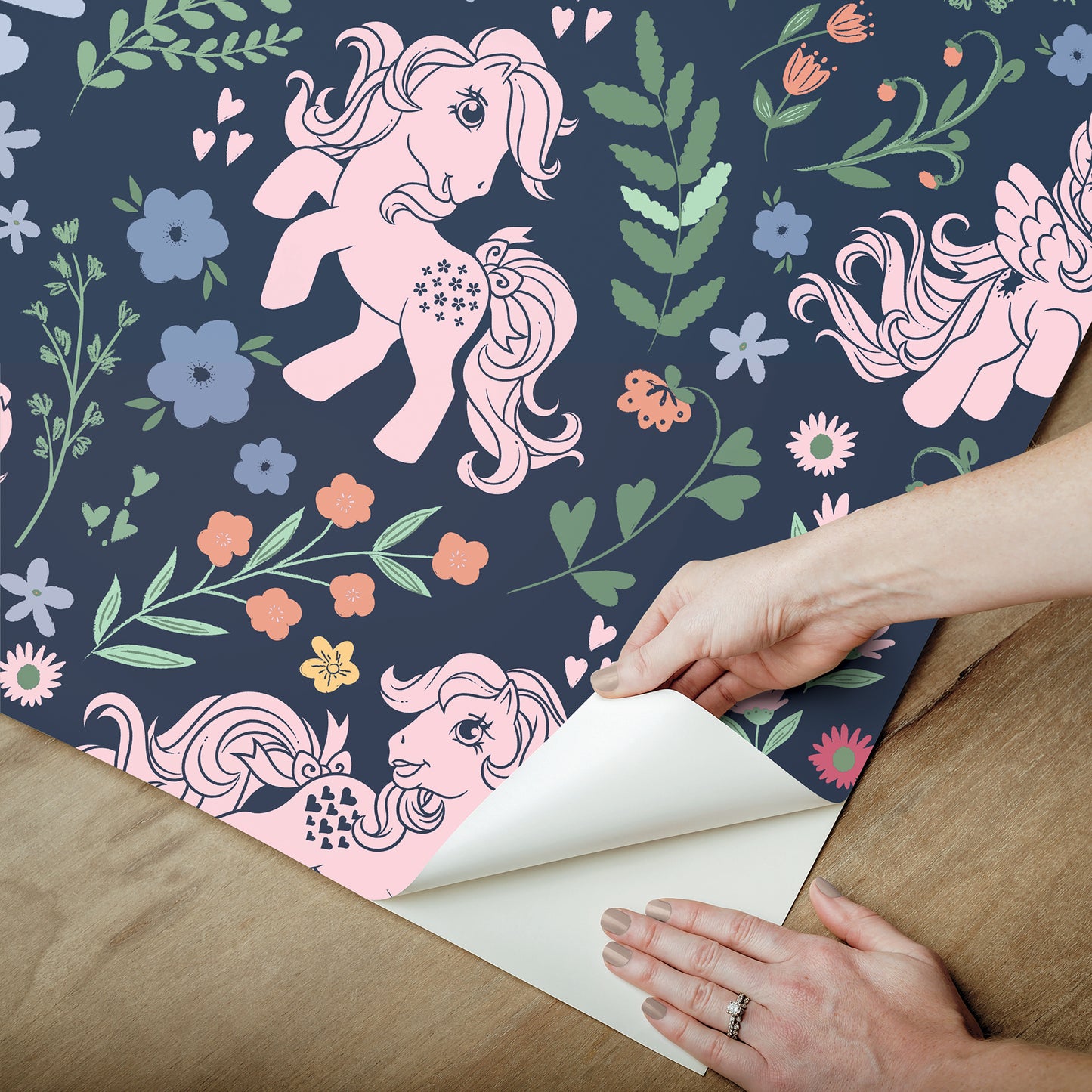 Navy wallpaper with pink unicorns & pastel flowers; being peeled back from corner by hands.