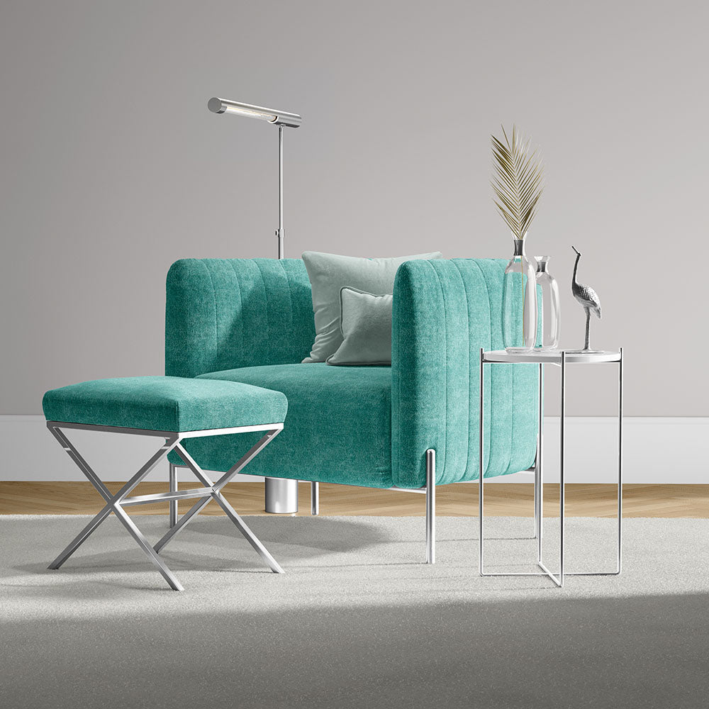 Teal velvet sofa with rounded arms and chrome legs, matching X-frame ottoman, glass-top side table and modern decor.