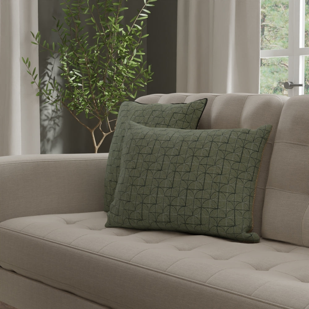 Beige tufted fabric sofa with two green geometric-patterned throw pillows; plant and curtains in a cozy living room.