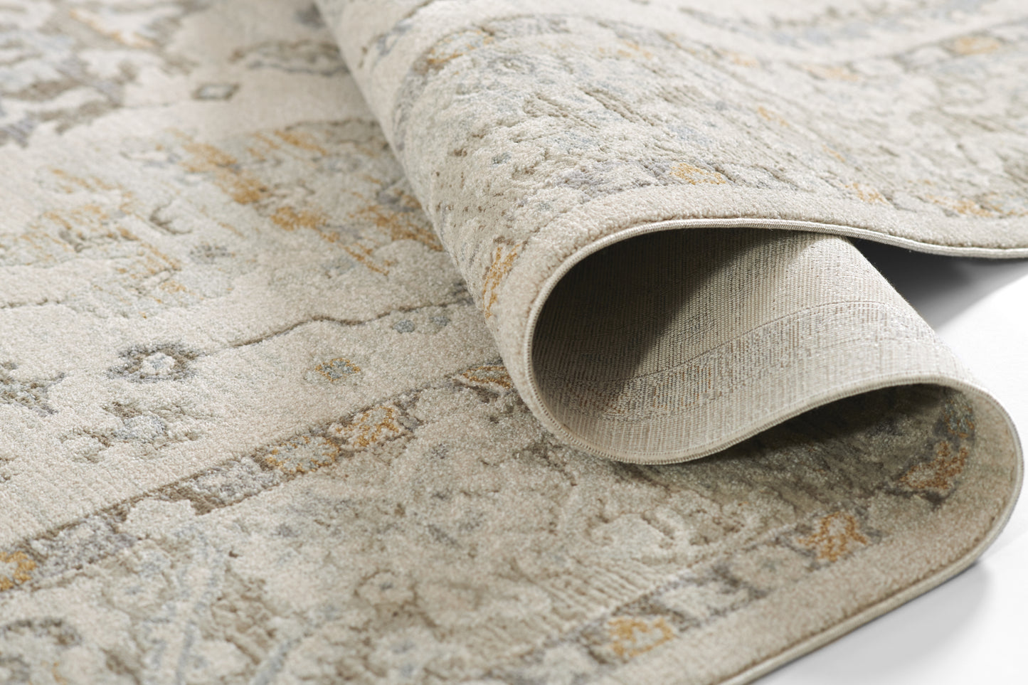 Beige patterned area rug with subtle blue and gold accents, rolled edge exposing soft woven pile.