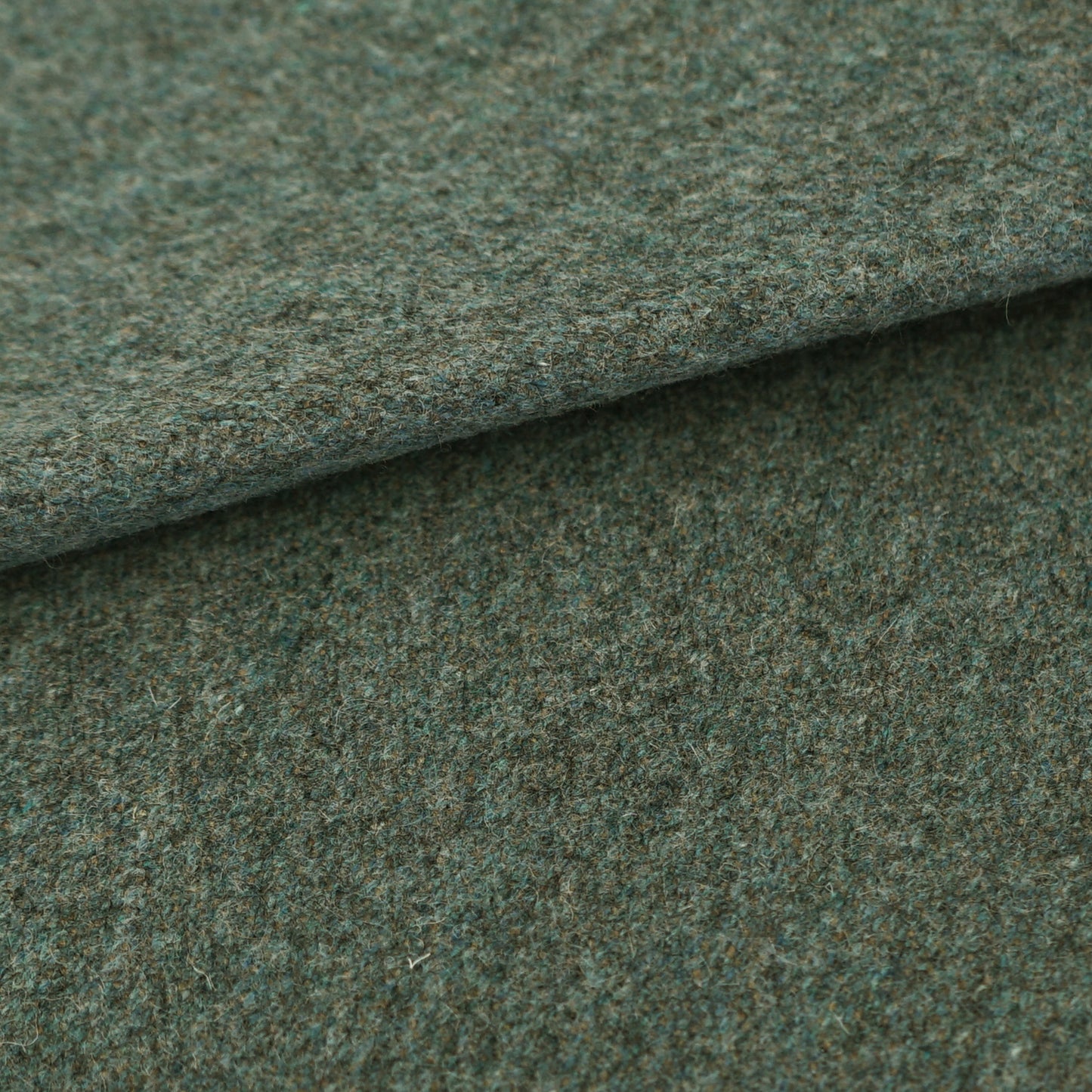 Close-up of blue wool fabric with a folded edge, showing a speckled, textured tweed-like surface.