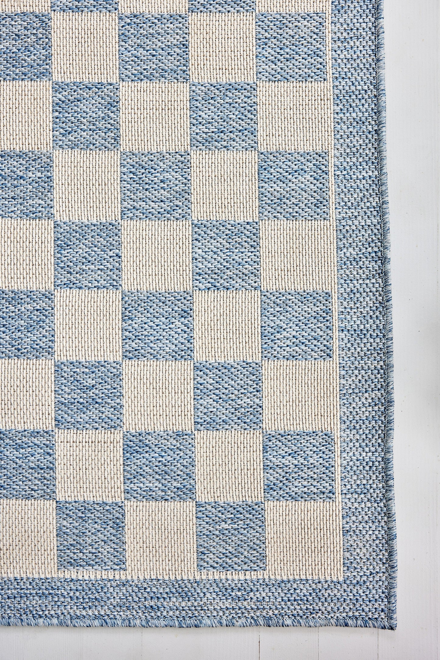 Rectangular woven rug with a blue and beige checkerboard pattern and blue border.