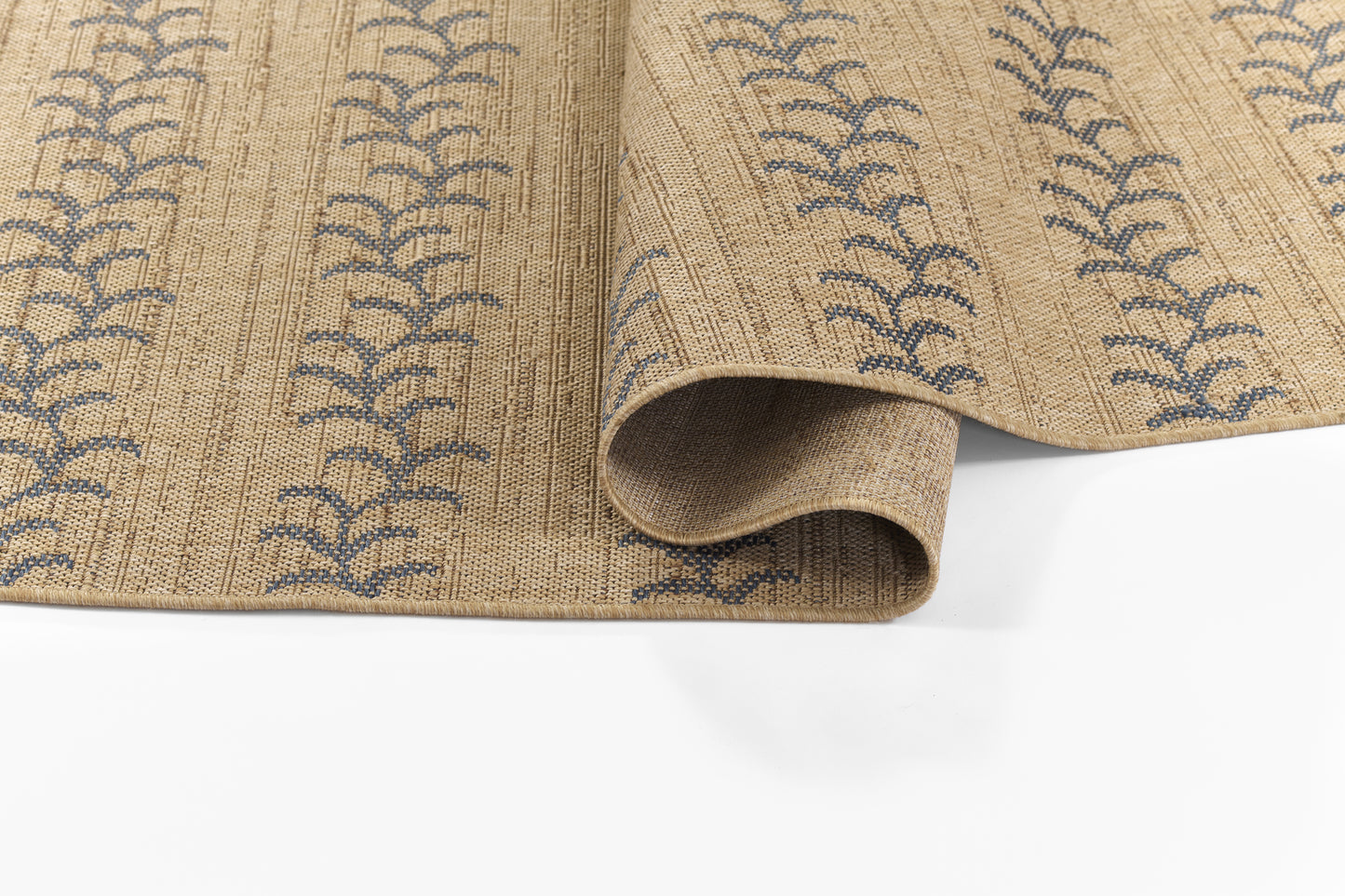 Beige woven rug with blue fern-like motifs, rolled edge showing thickness and natural fiber texture.