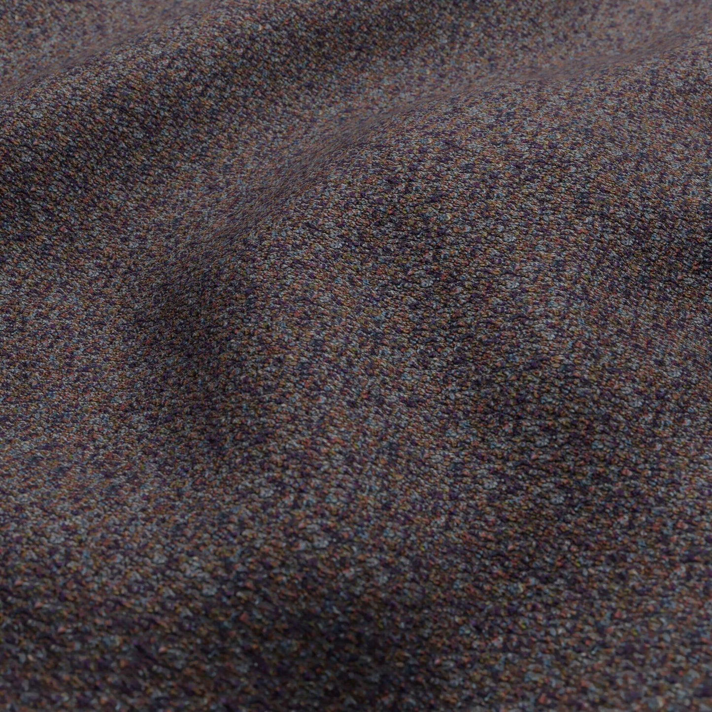 Close-up of bouclé fabric in dark blue, rust, olive green and plum tones, showing a textured surface with soft draped folds.