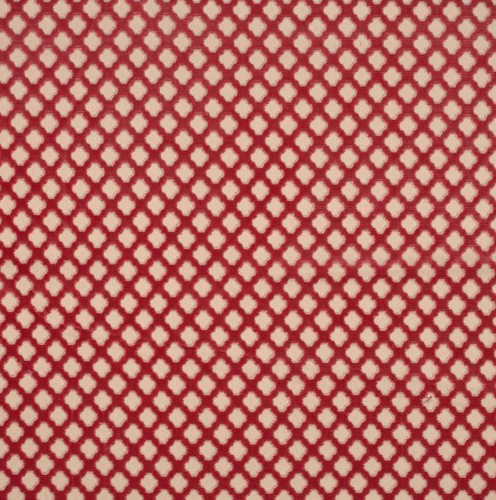 Red fabric with cream small quatrefoil motifs forming a repeating lattice pattern.