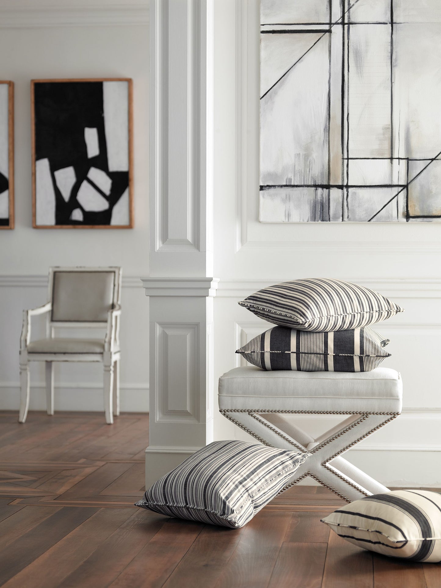 White paneled living room with an ivory X-frame ottoman and striped black & white cushions.