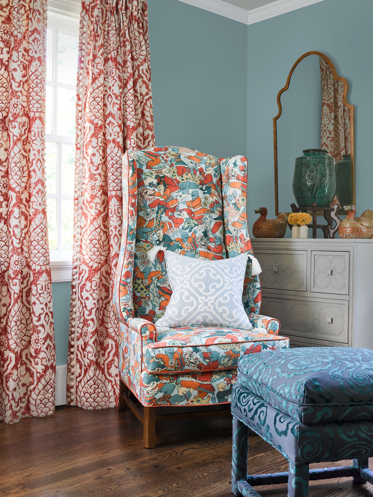 Colorful teal, orange and white patterned wing chair with light blue pillow, paired with a blue patterned ottoman.