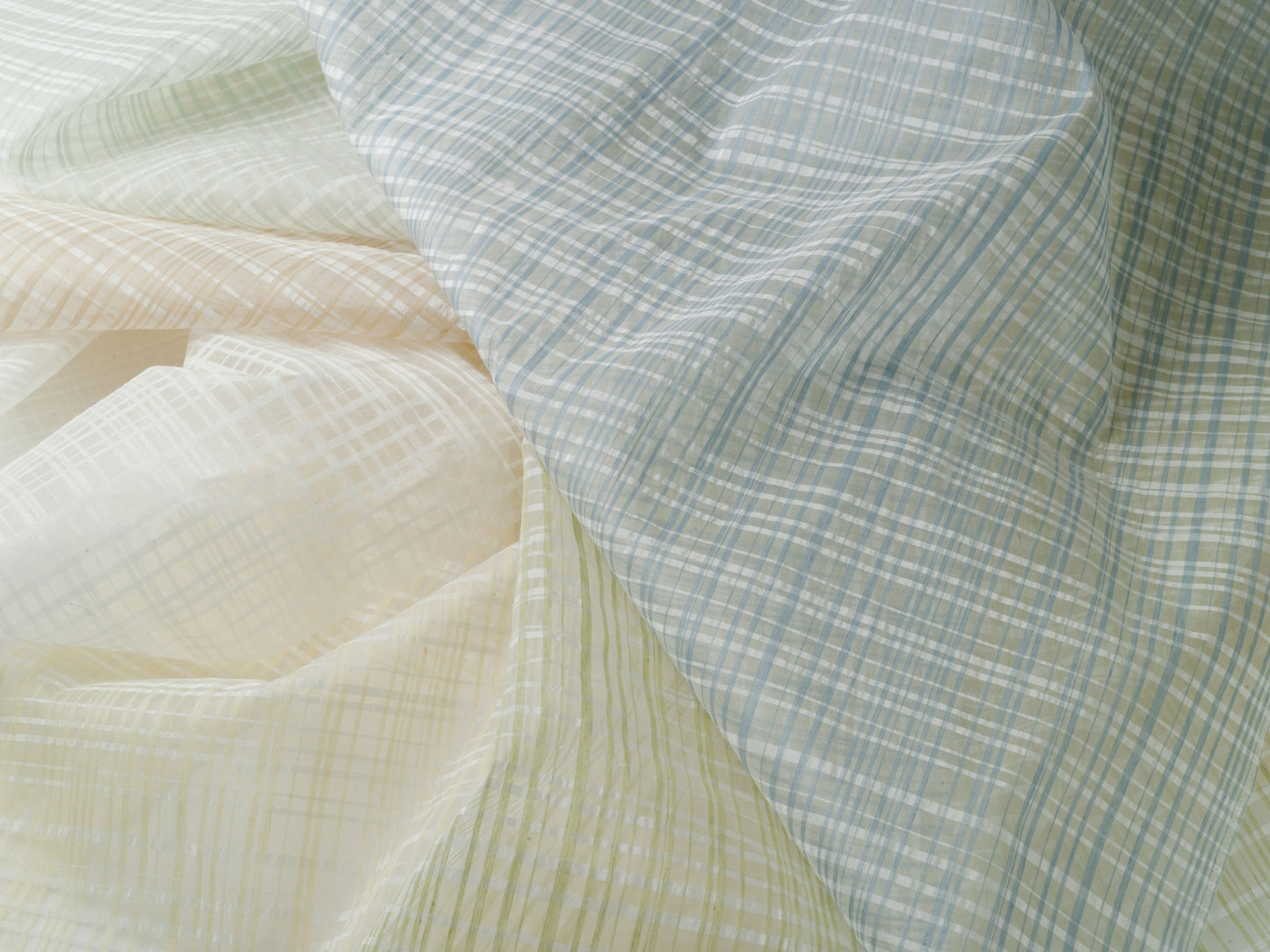 Soft pastel plaid cotton fabric in blue, cream and pale yellow, with fine check pattern and gentle drape.