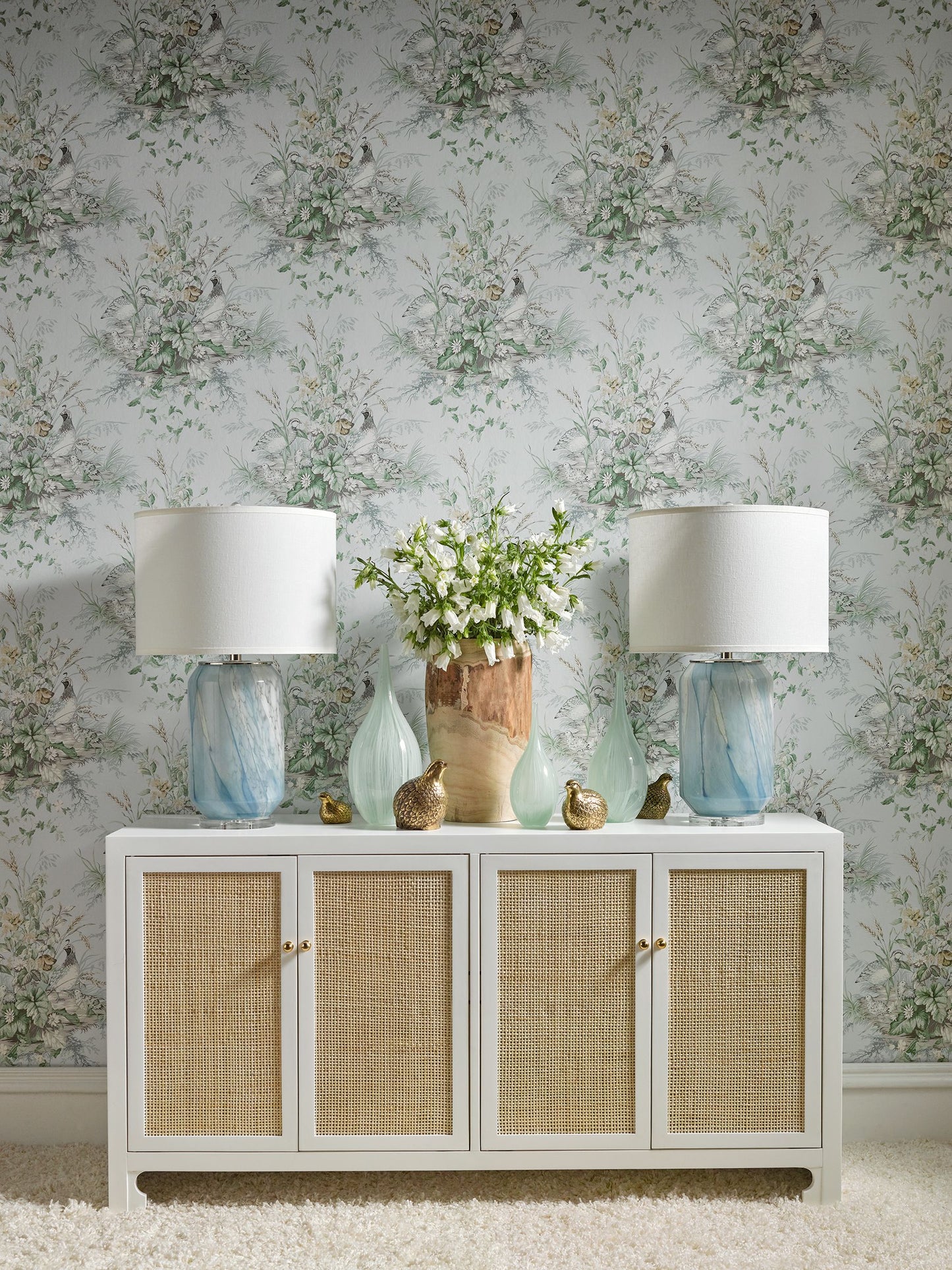 White console with four wicker-panel cabinets, blue glass lamps on each end, vase of white flowers, coastal chic decor.