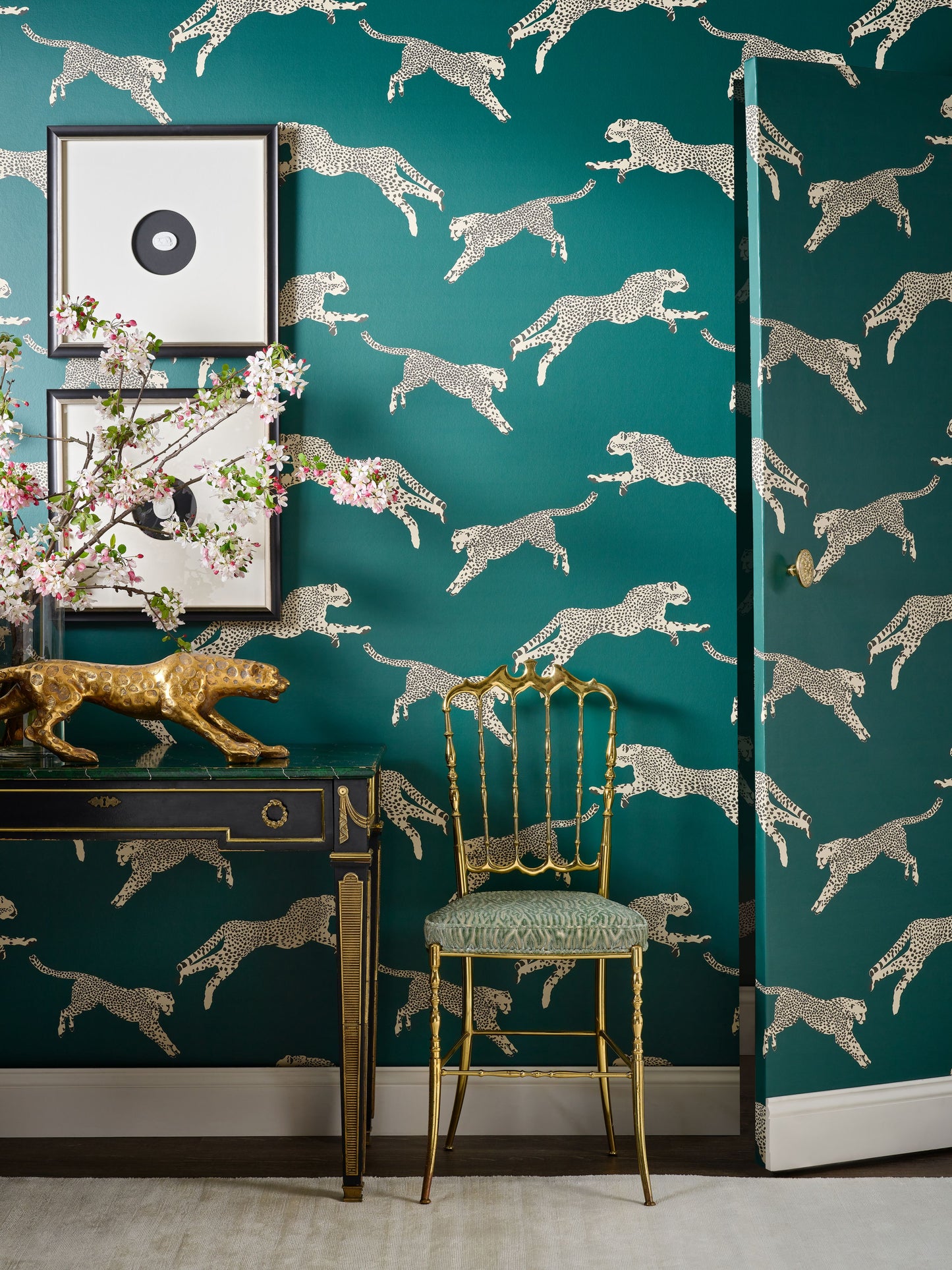 Teal wallpaper with metallic silver cheetah silhouettes; gold console table with framed art and a gold chair.