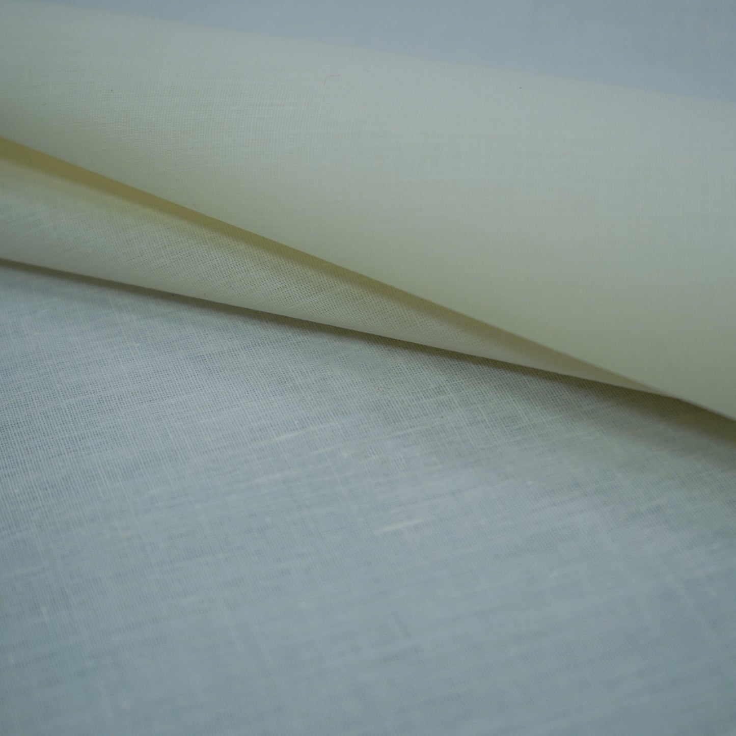 Cream offwhite plain lining fabric roll with a natural woven texture, draped on a pale blue backdrop.